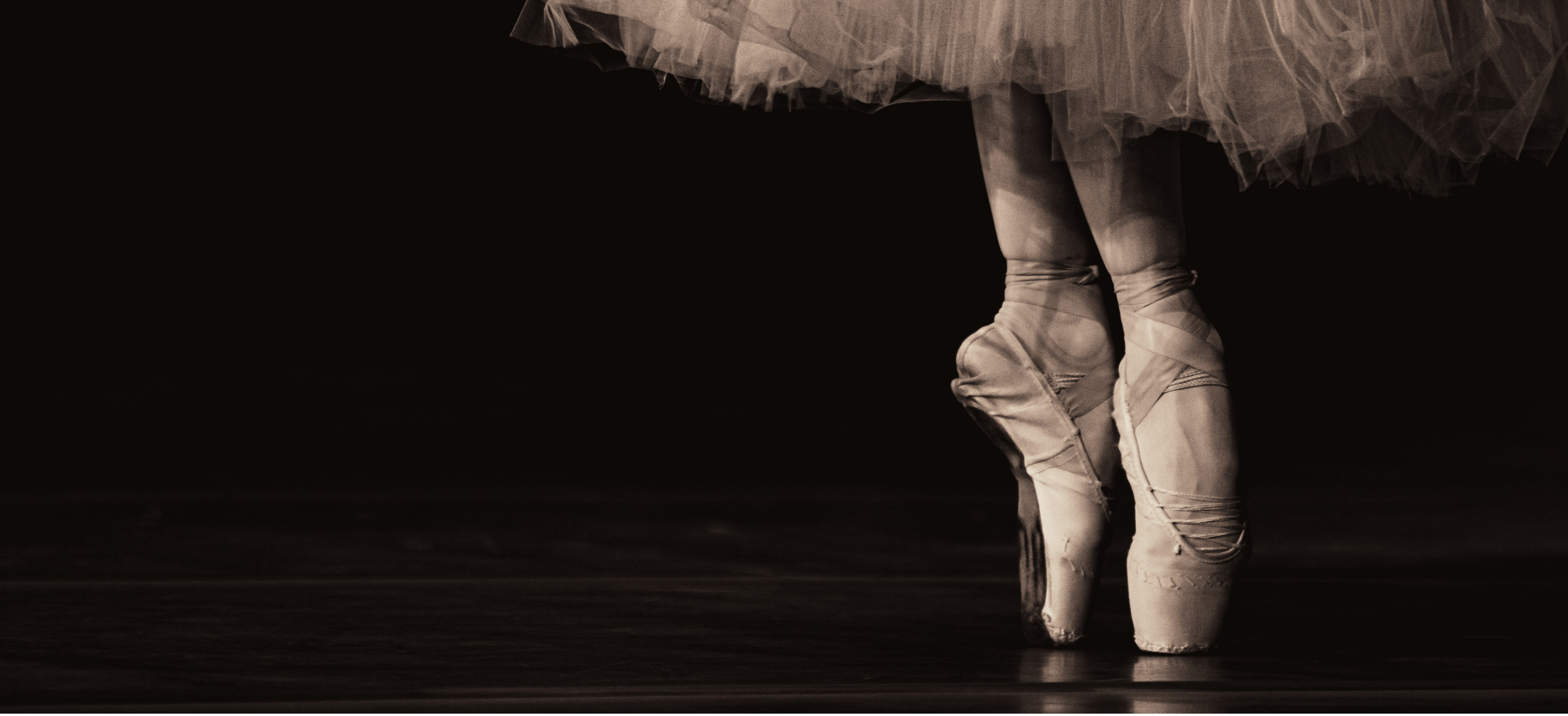 Ballerina's feet in pointe shoes with a tutu on a black background
